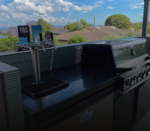 Keg fridge and tap tower built into an outdoor kitchen beside a barbecue